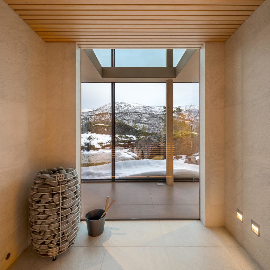 A room inside a cabin facing some large windows on the opposite side, with the mountain as a view.